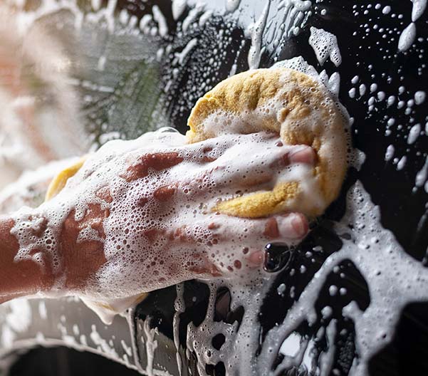 Detail shot of a hand holding a sponge and washing a black car.